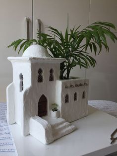 a plant in a pot on top of a white table next to a small house