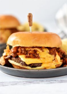 a cheeseburger on a plate with potato chips in the background and a toothpick sticking out of it