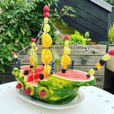 a watermelon boat made out of fruits and berries on a white table outside