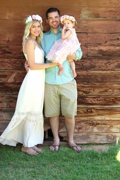 a man and woman holding a baby in front of a wooden wall