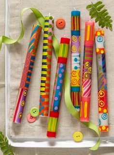 several different colored pens and buttons on a white tray next to green ribbon, leaves and button holes