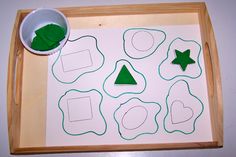 a wooden tray with cut out shapes and green felt on it, next to a white cup