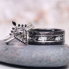 two wedding bands with black and white diamonds on them sitting on a rock next to each other