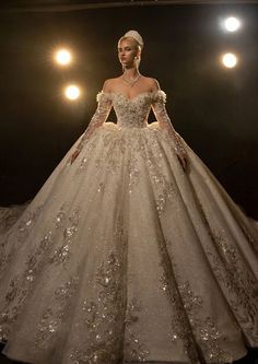 a woman in a wedding dress with long sleeves and pearls on the skirt is standing in front of spotlights