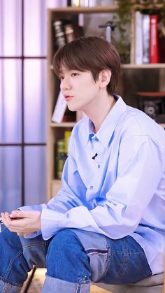 a young man sitting on top of a wooden bench in front of a book shelf