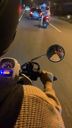 a person on a motorcycle driving down the street at night with other cars behind them