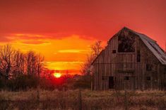 the sun is setting behind an old barn