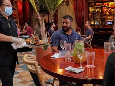 people sitting at a table with food and drinks in front of them wearing face masks