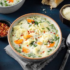 a bowl of soup with carrots, spinach and cheese in it next to two spoons