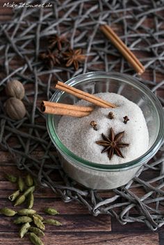 a bowl filled with white powder and cinnamons on top of a wooden table next to nuts