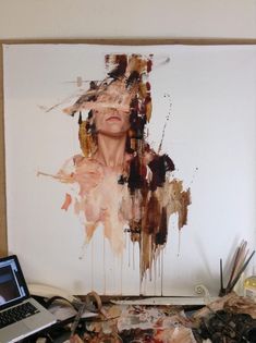 an art work is being displayed on a table next to a laptop and paintbrushes