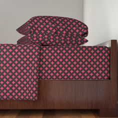 a bed with pink and black bedspreads on top of wooden headboard next to white wall