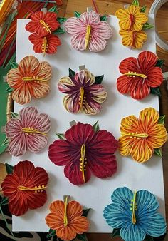 many different colored flowers are on a white board with some scissors and thread in the background