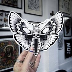 a person holding up a sticker with a butterfly on it's face in front of a wall full of pictures