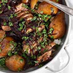 a pot filled with meat and vegetables on top of a white table cloth next to a spoon