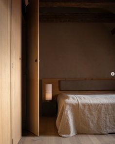 a bed sitting in a bedroom next to a wooden cabinet and wall with a light on it