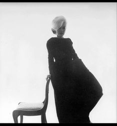 an old black and white photo of a woman leaning on a chair with her back to the camera