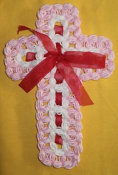 a crocheted pink and white cross with a red ribbon around it on a yellow background