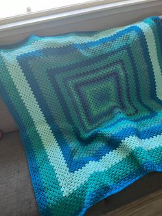 a blue and green crocheted blanket sitting on top of a window sill