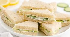 several sandwiches on a plate with cucumbers and lemon wedges in the background