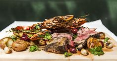 steak, potatoes and shrimp on a wooden cutting board with garnishes in the background