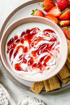 a bowl of dip with strawberries and crackers on the side