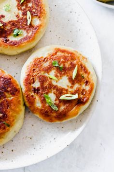 three small pizzas sitting on top of a white plate next to a bowl of pickles