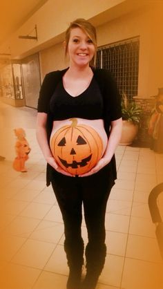 a pregnant woman holding a pumpkin in her belly while wearing a black shirt and leggings