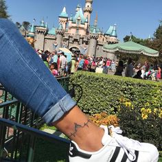 a woman's foot with a tattoo on her left ankle in front of a castle