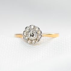 an antique diamond ring sits on a white surface, with the center stone set in yellow gold