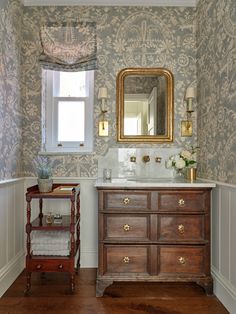 a bathroom with wall papered walls and a wooden dresser in the corner, along with a mirror on the wall