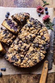 blueberry crumb cake sliced on top of a cutting board next to some flowers