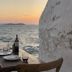 a table with plates and wine glasses on it near the water's edge at sunset