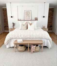 a bed with white blankets and pillows in a bedroom next to a wooden bench on the floor