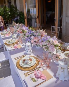 the table is set with pink and white flowers in vases, plates, and napkins