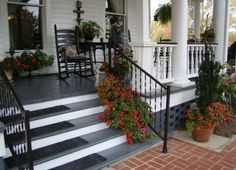 front porch with flowers and rocking chairs on the steps, potted geranias