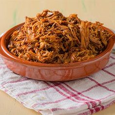 a bowl filled with shredded meat sitting on top of a table next to a fork