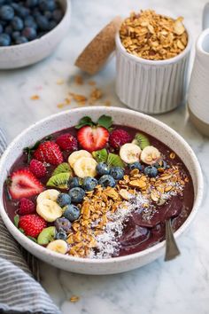 a bowl filled with fruit and granola on top of a table next to two cups