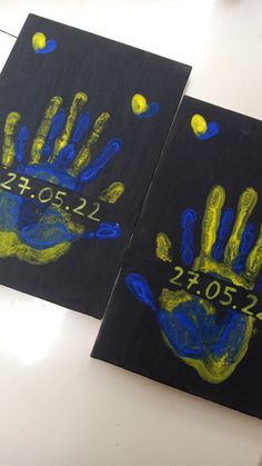 two handprints on black paper with yellow and blue paint