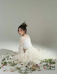 a woman sitting on the ground with flowers in her hair and wearing a white dress