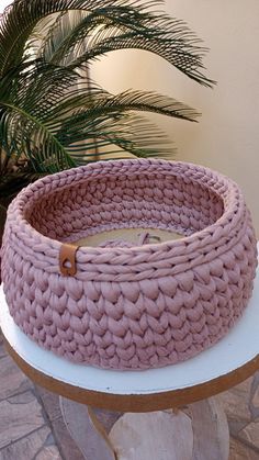 a pink knitted basket sitting on top of a table next to a potted plant