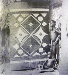 an old black and white photo of two men standing in front of a wall quilt