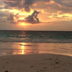 the sun is setting over the ocean with clouds in the sky and footprints in the sand