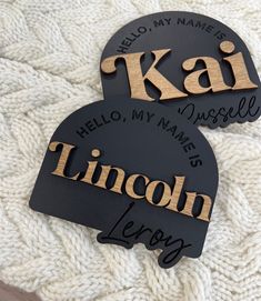 two black and gold personalized name tags on a white knit blanket with the words, kal hello my name is lincoln leroy