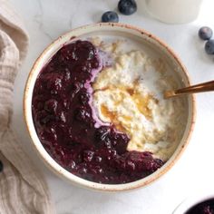 a bowl filled with oatmeal and blueberries next to a glass of milk