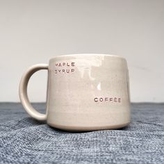 a white coffee mug with the words maple syrup on it sitting on a blue cloth