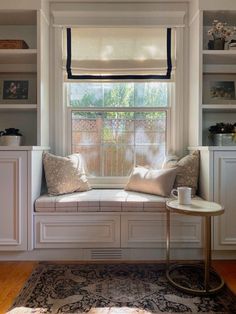 a window seat in the corner of a room with white cabinets and pillows on it