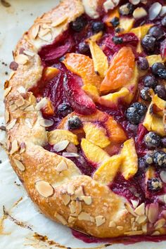 a fresh fruit pizza with almonds, blueberries and peaches on top is ready to be eaten