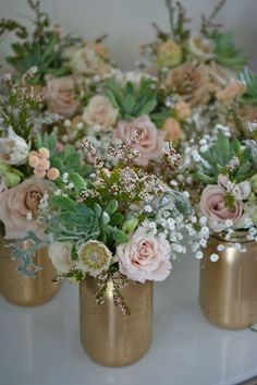 three gold vases filled with flowers on top of a table