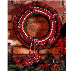 a red and green christmas wreath hanging on the side of a brick wall next to pine cones